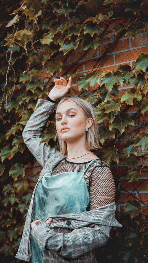 a young woman stands in front of a ivy wall