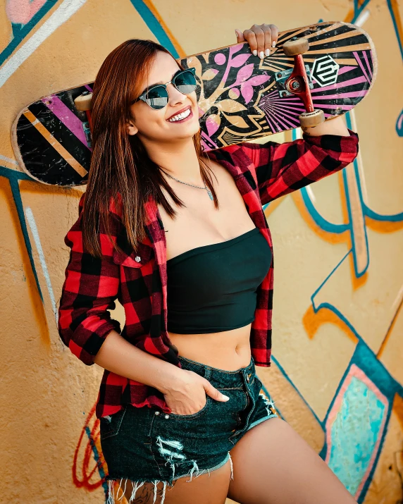 young woman in red and black checkered shirt holding skateboard and smiling