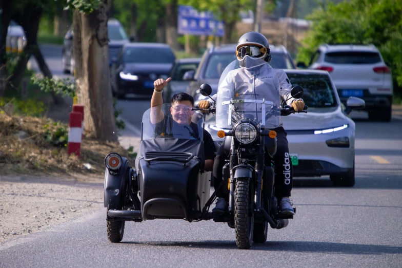 two people riding motorcycles on a street with cars in the background