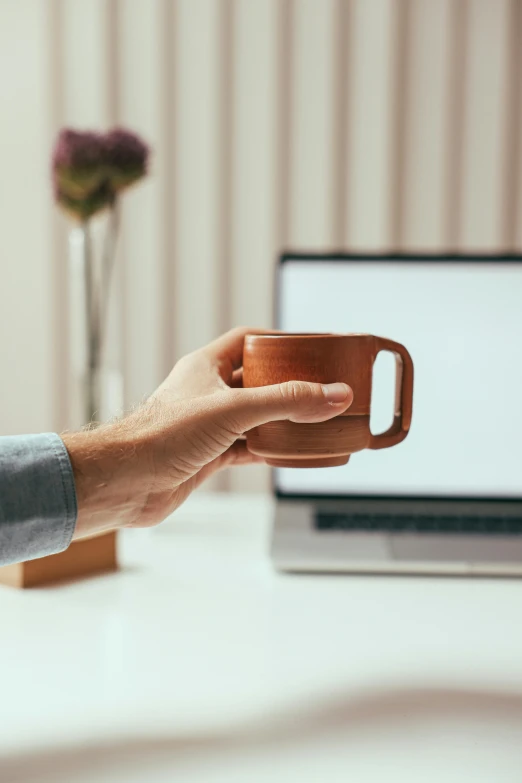 a person's hand holding a brown mug over a white desk