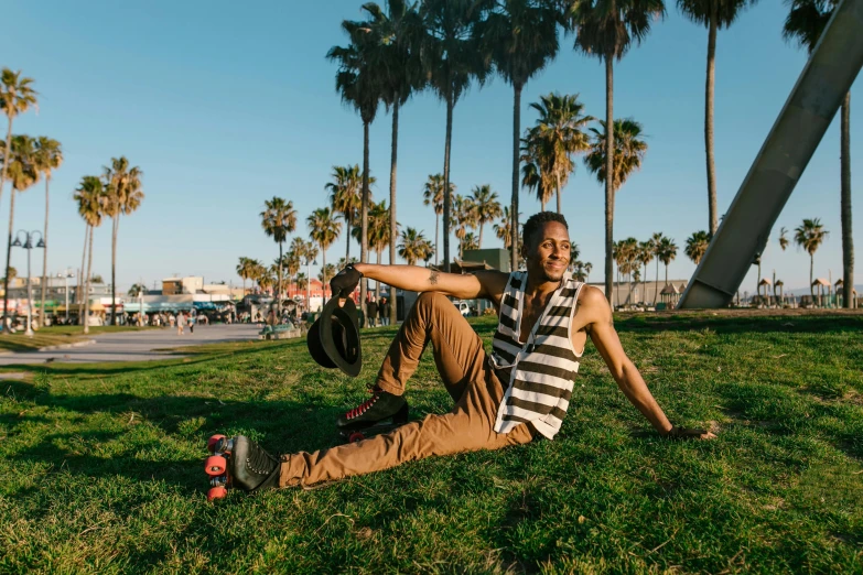 a man in striped shirt and jeans sitting on grass near palm trees