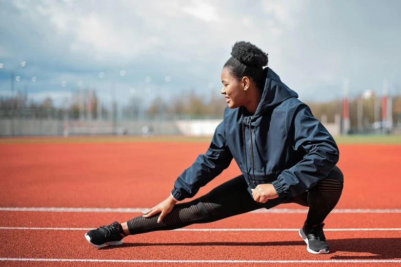 a black woman crouches on the edge of a red running track