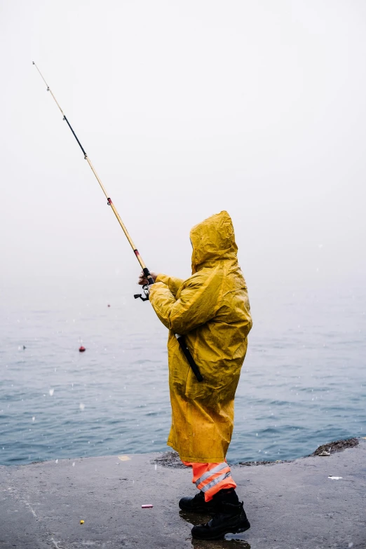 person in yellow rain jacket fishing off the edge of ocean