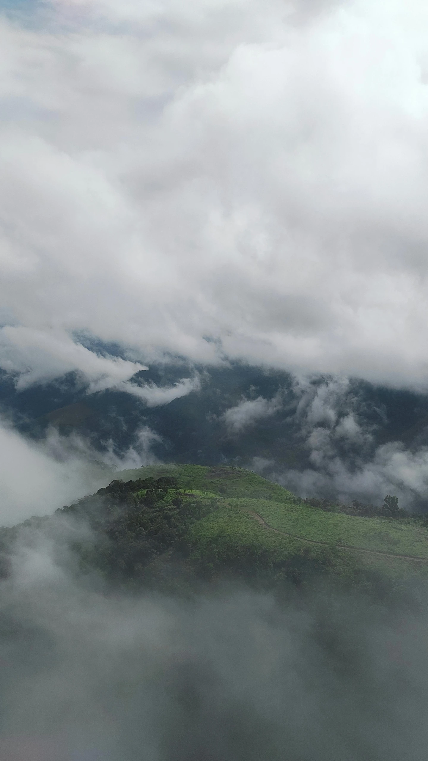 an area with a green mountain surrounded by clouds