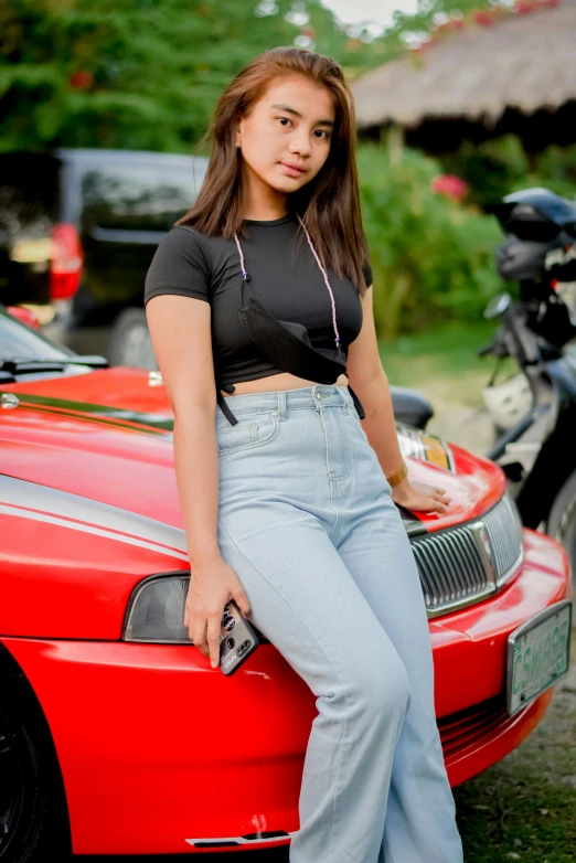 a young woman poses in front of her red sports car