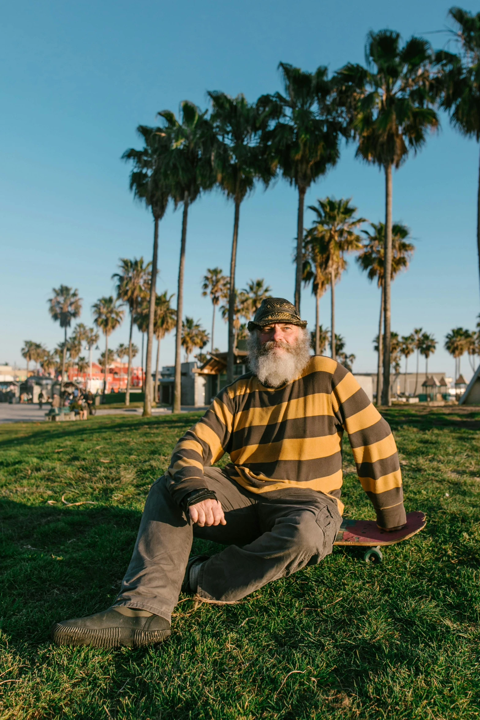 a bearded man is sitting on a skateboard in the grass