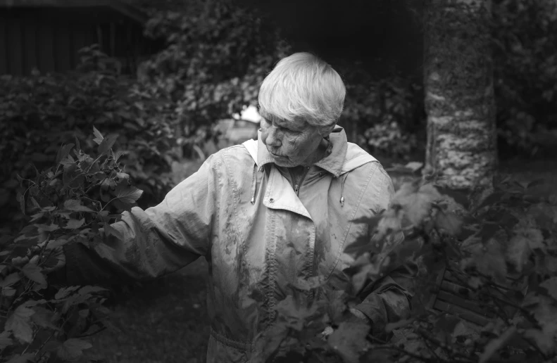 a woman wearing an over - sized coat and looking at plants