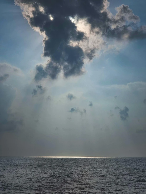 large gray clouds with sun over ocean and boat