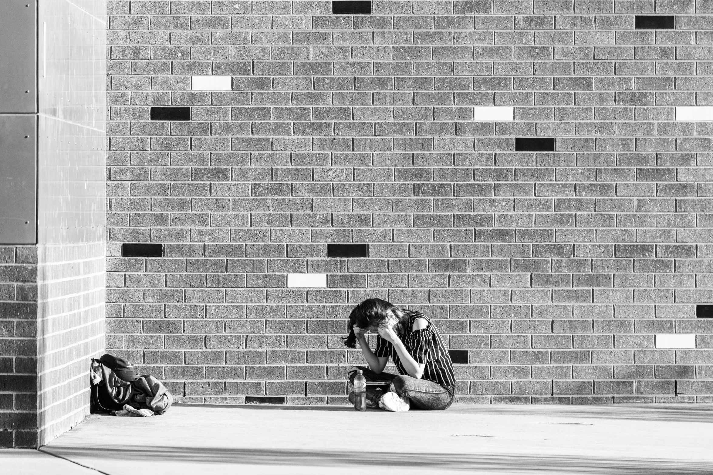 a woman sitting on the ground with her head down while talking on a cell phone