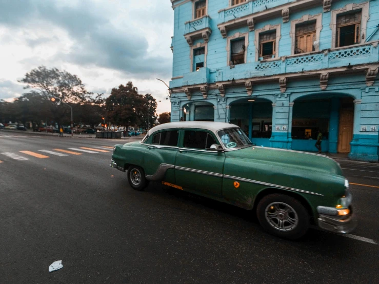 a green car driving down the middle of a street