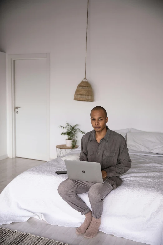 a man sitting on his bed while working on a laptop