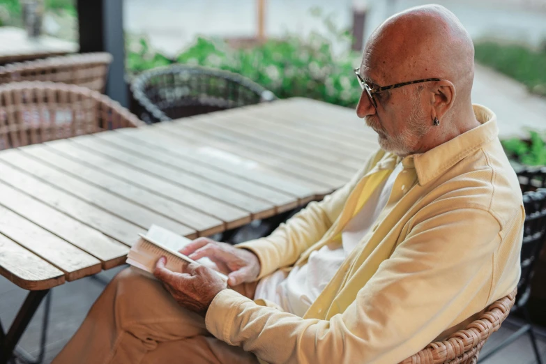 man sitting at outdoor cafe table reading a book