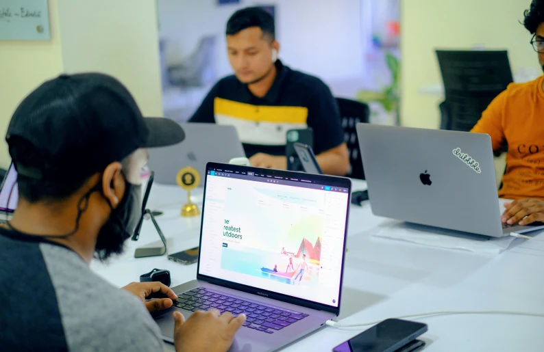 four people sitting around a table with two laptops