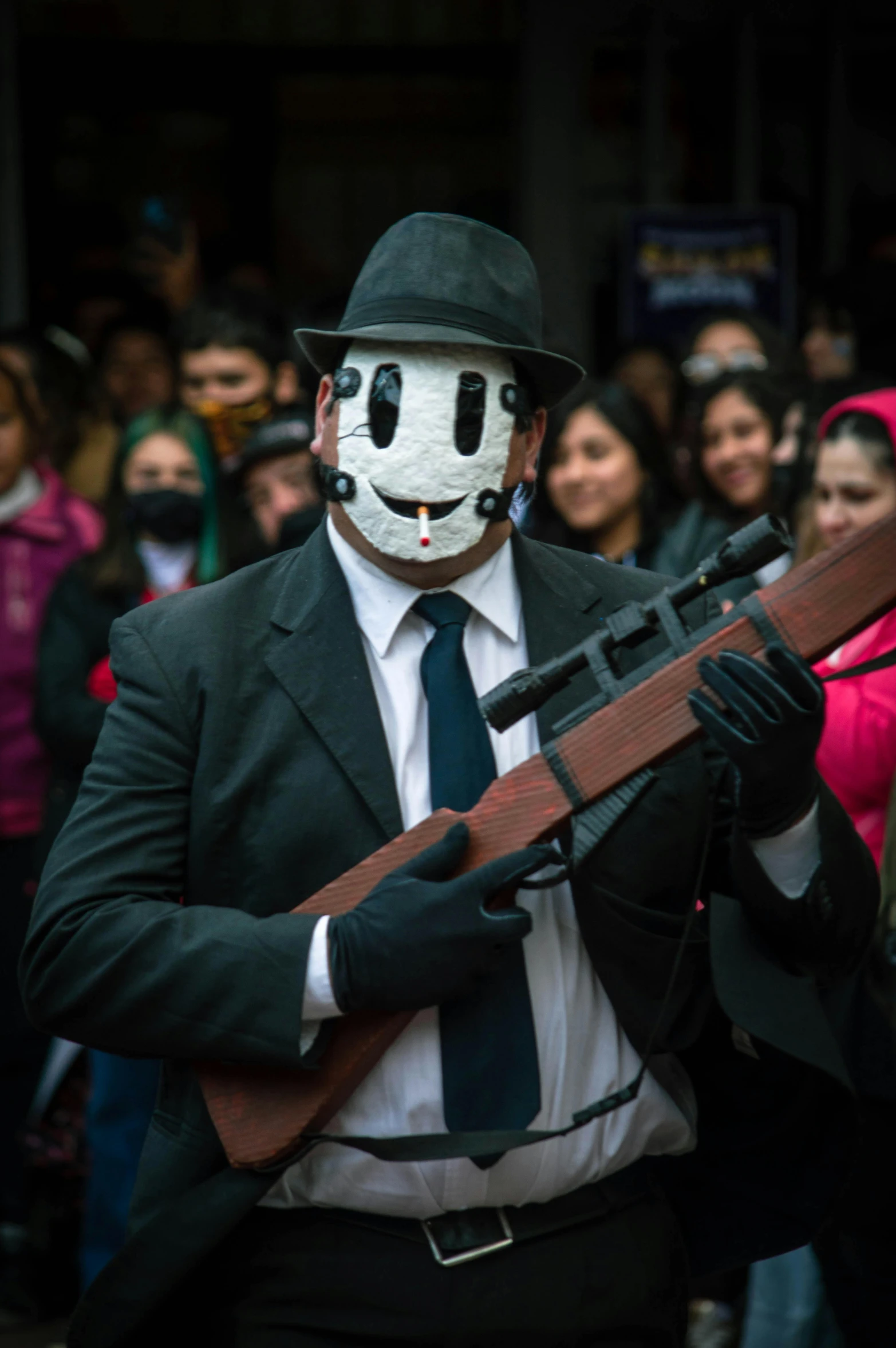 a man in white mask and a suit with a gun