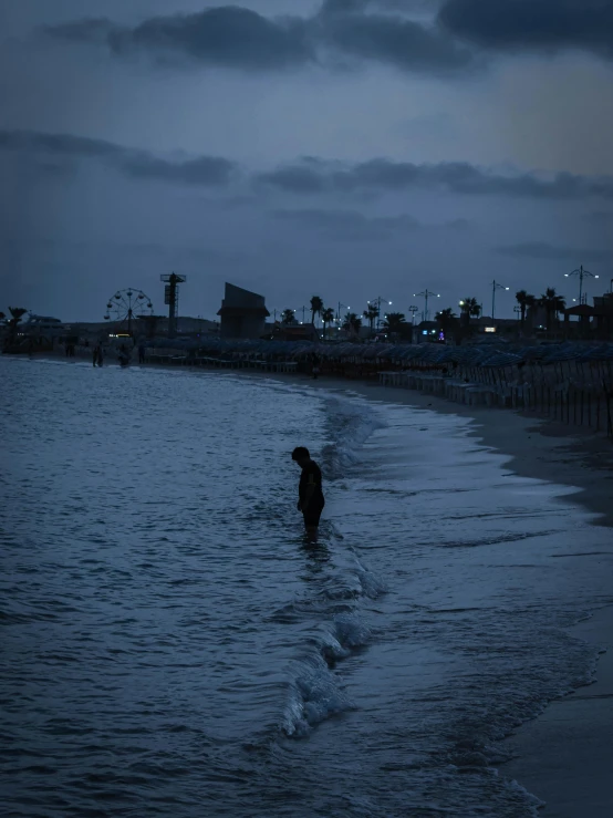 person walking on the beach during dusk, with city in background