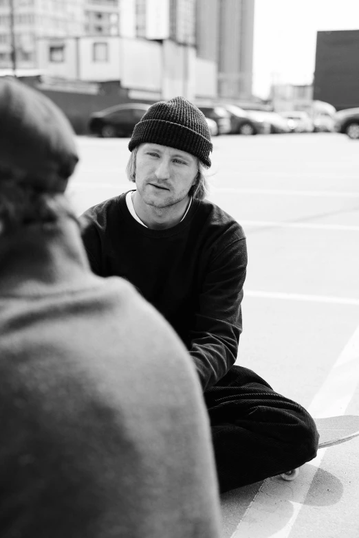 two men talk outside, one wearing a hat and one in a sweater