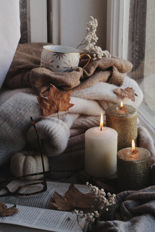 three lit candles are on a pile of knits next to a cup