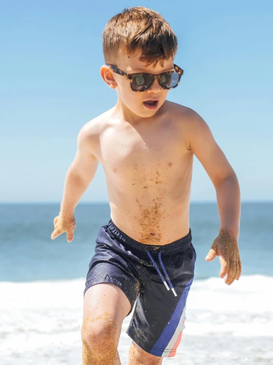 a little boy running on the beach in sunglasses