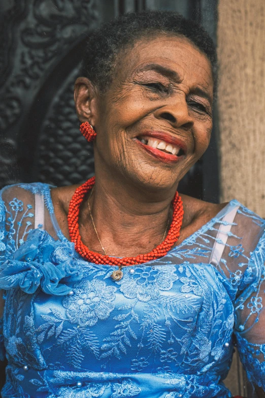 woman smiling wearing blue shirt with red beads