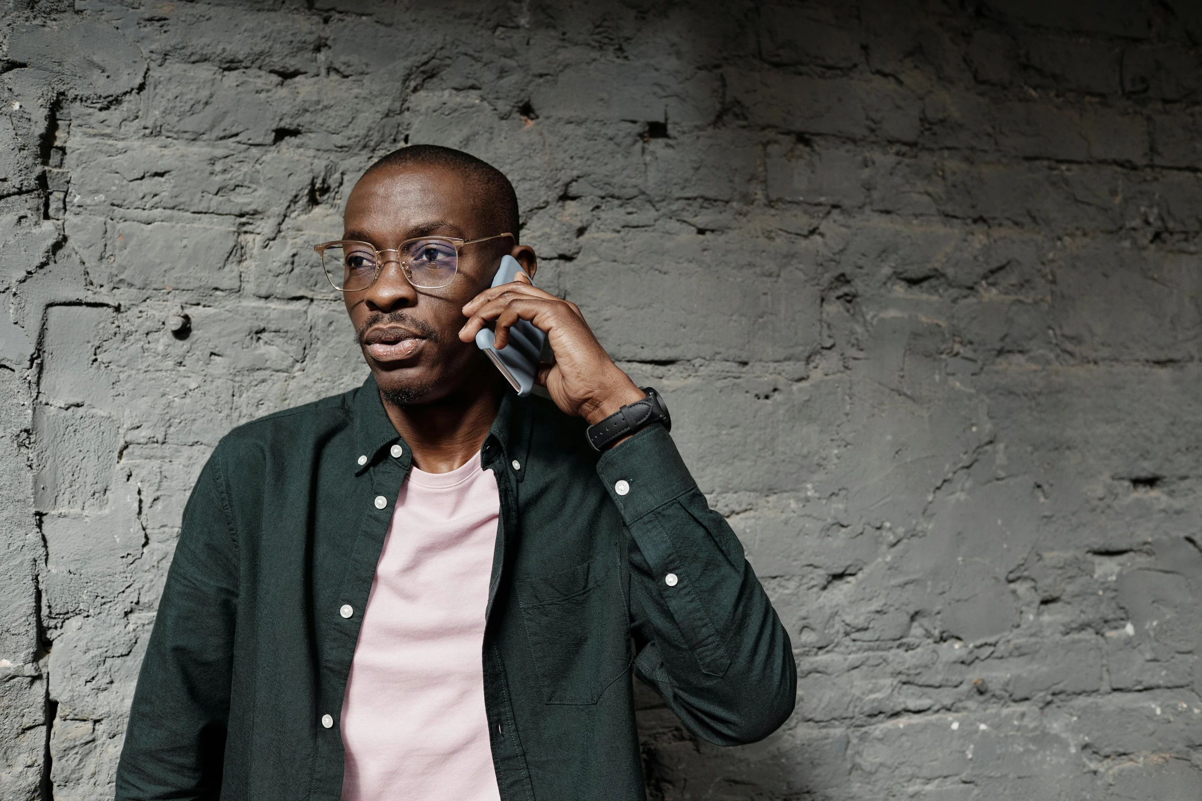 a man with glasses and a cardigan talks on a cellphone