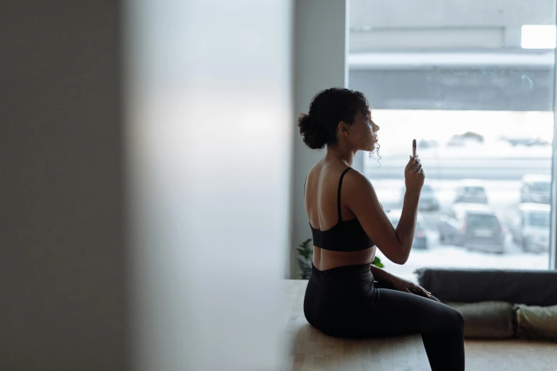a woman sitting on a windowsill wearing black workout clothing