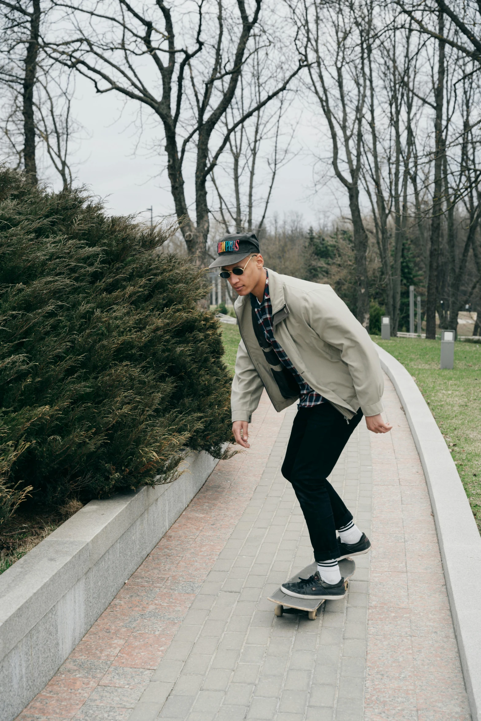 man wearing hat and glasses riding on skateboard on path in urban park