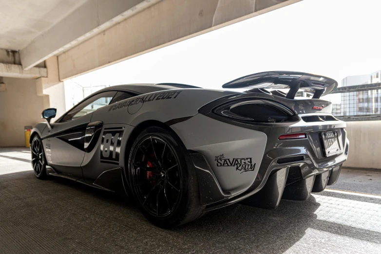 a silver sports car with black wheels sitting under a bridge