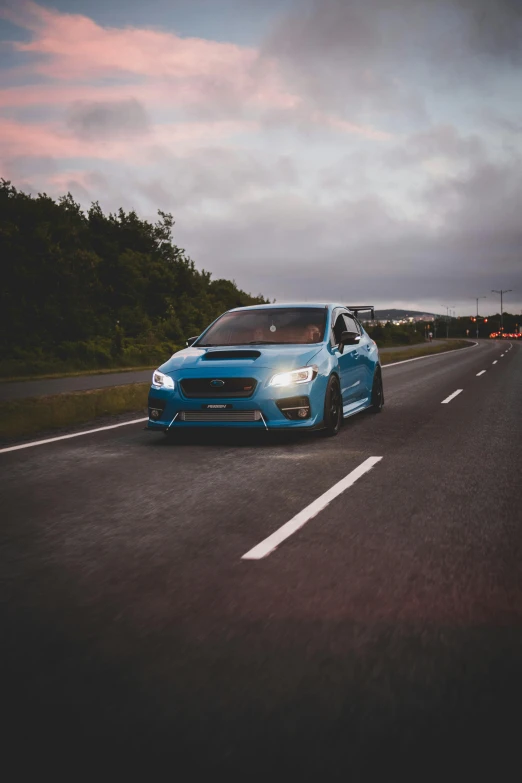 a blue subarunt is on the highway in the evening