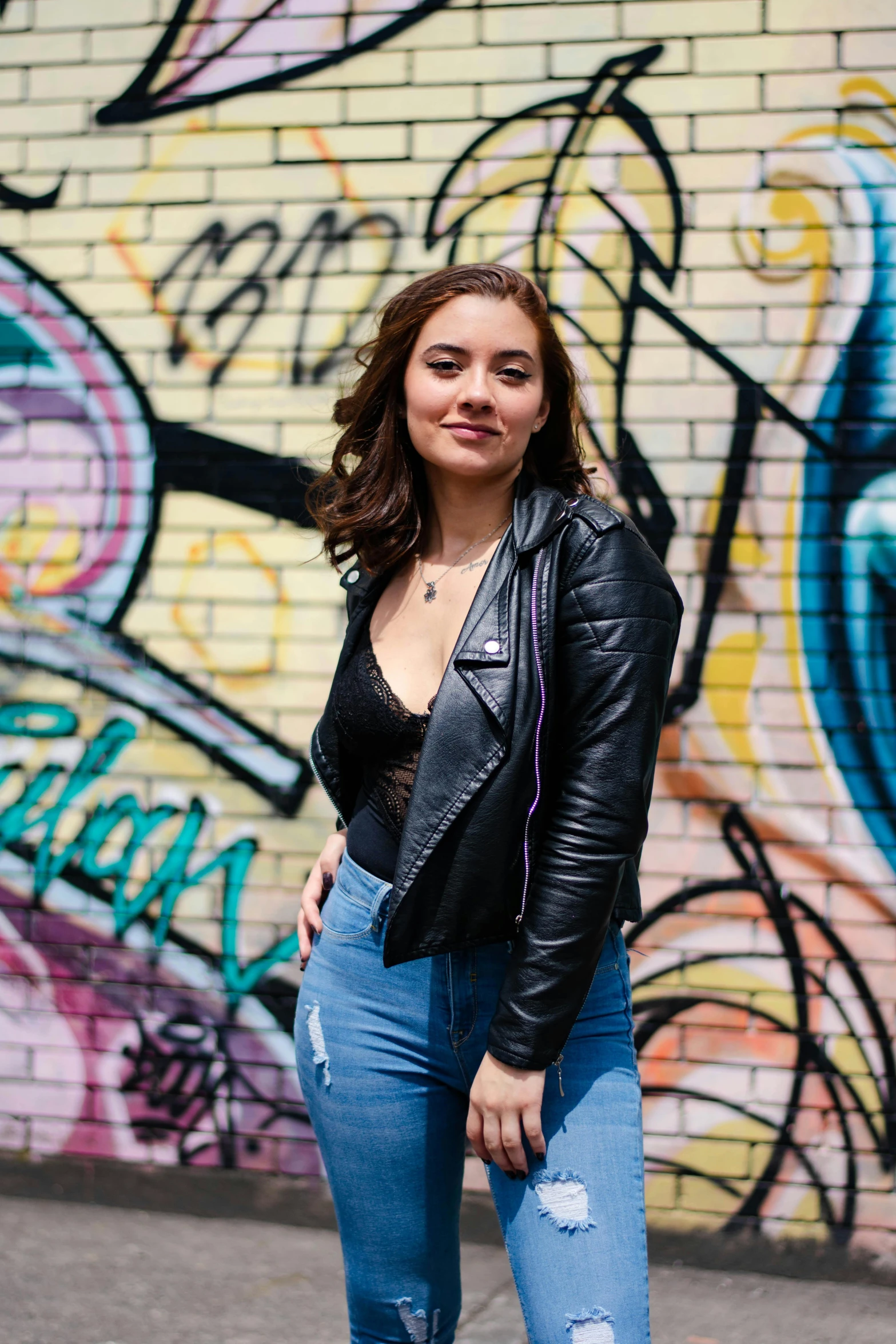 a woman in a leather jacket standing in front of a graffiti wall