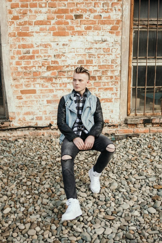 a man in black jeans sitting on a brick wall