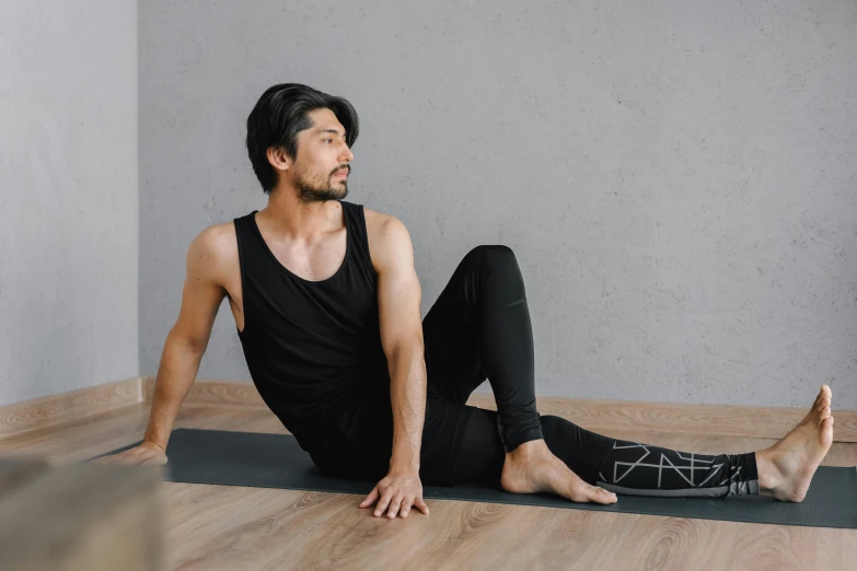 man in yoga pose looking back while sitting on his yoga mat