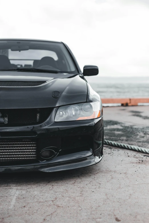 a modified black car sits on the concrete by the water