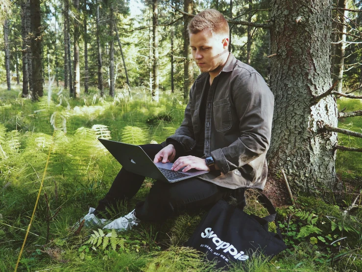 man on his laptop in the woods with many backpacks