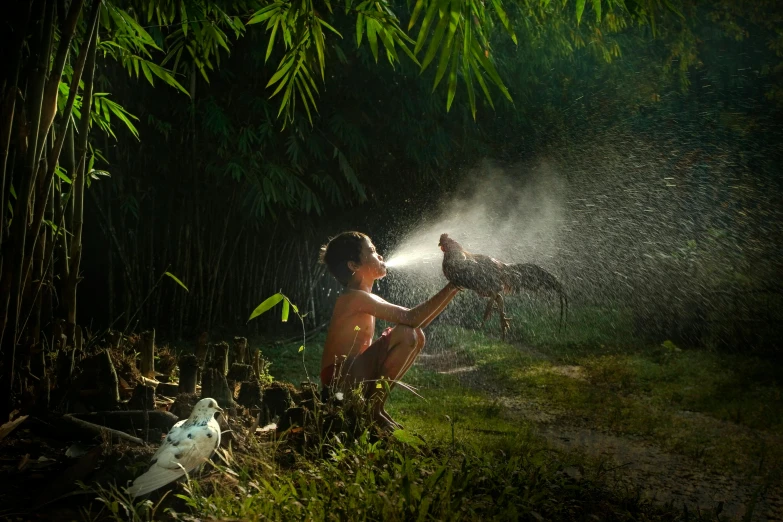 a young man playing with a large bird in the woods