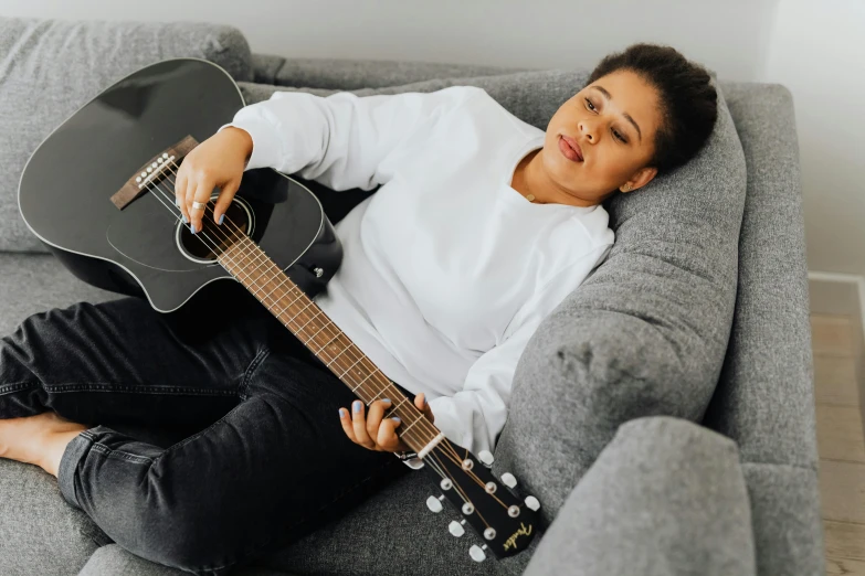 a young lady with a guitar is laying on the couch