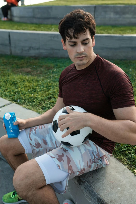 a man sitting on the curb next to a ball with a bottle