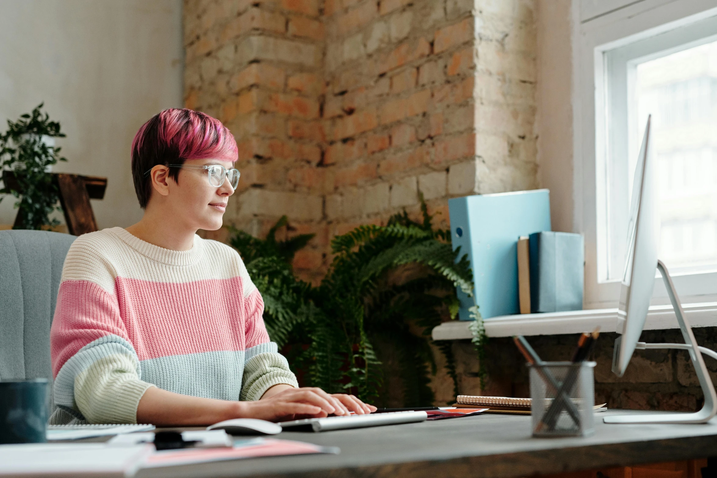 a girl with red hair, glasses and a sweater using a computer