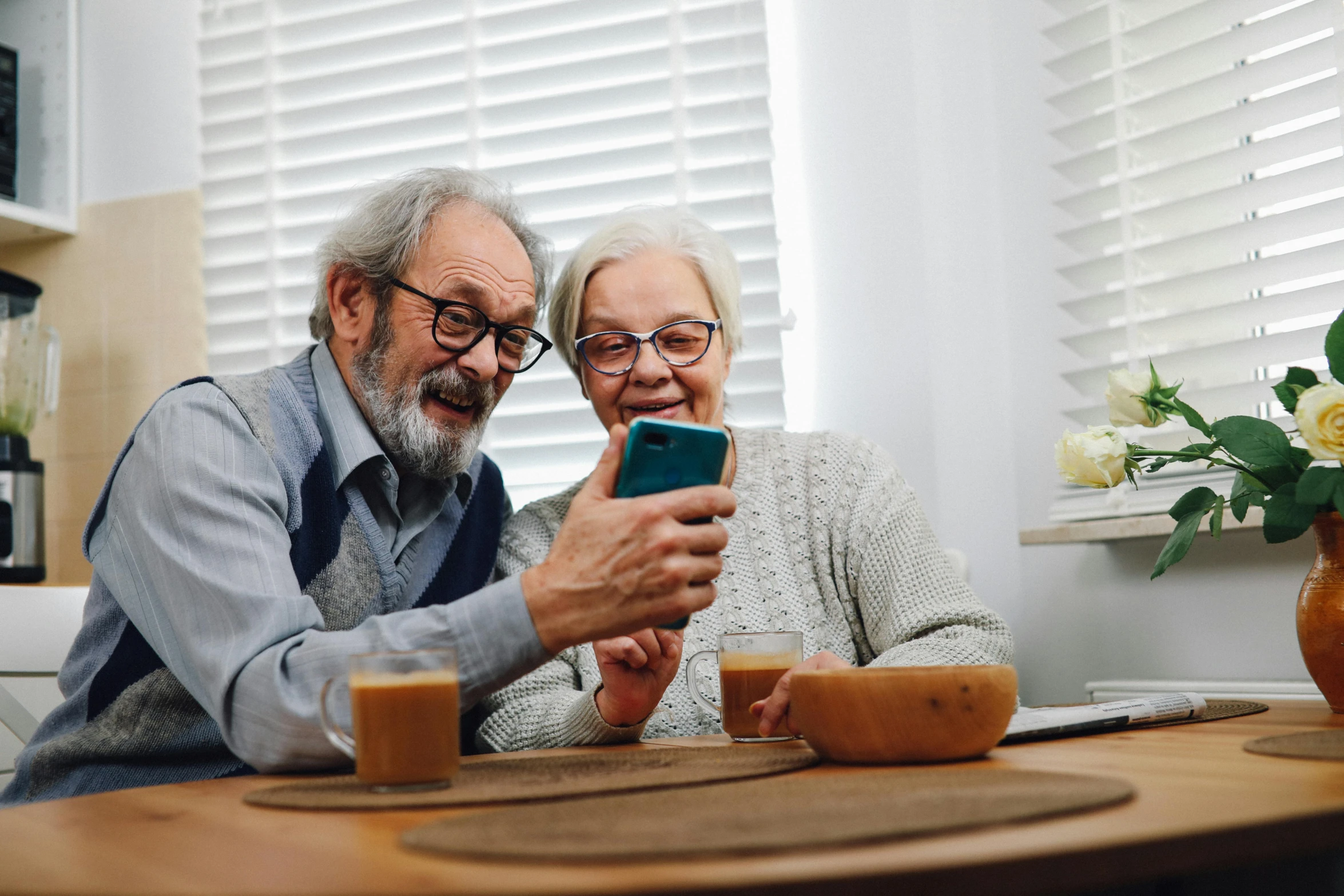 two people in glasses sit at a table and look at a phone