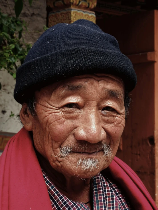 an older man with mustache and beanie is wearing a red scarf