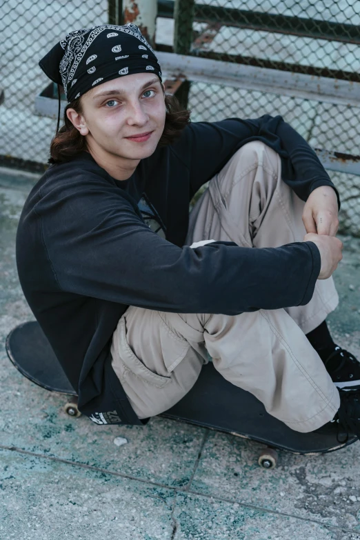 a young man sitting on his skate board wearing his cap