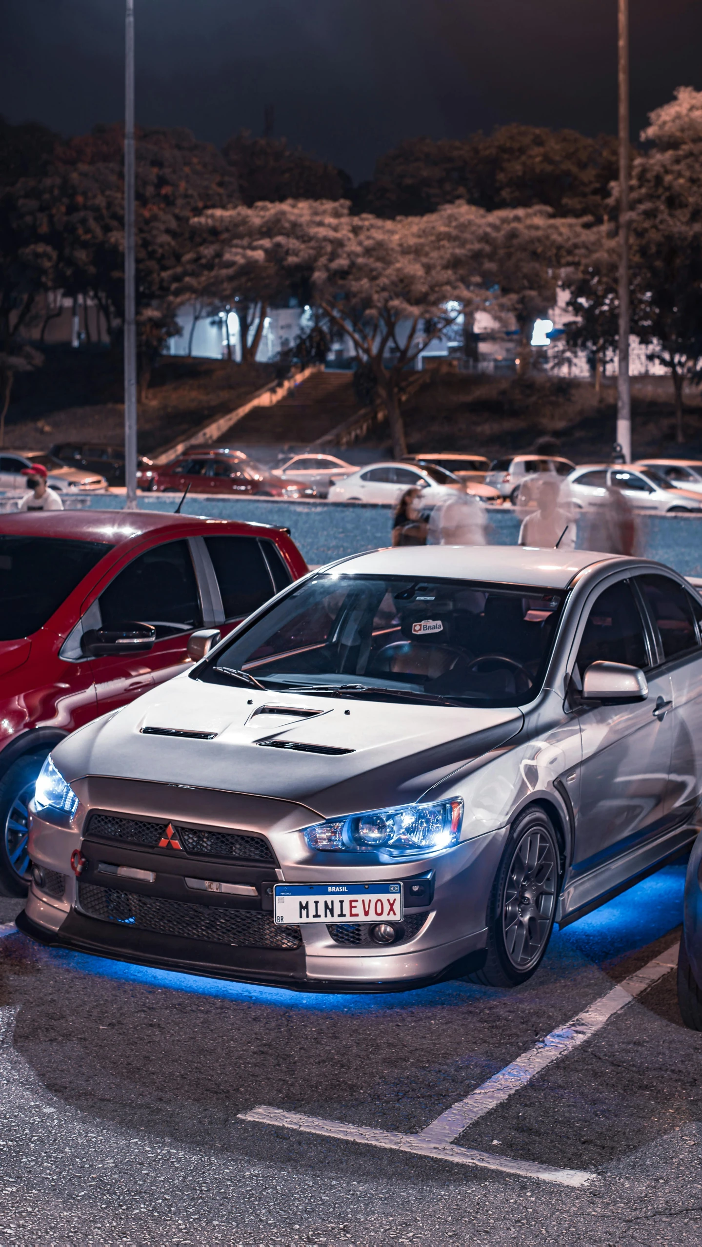 two silver cars parked in a parking lot with other cars