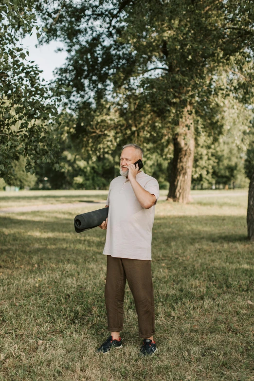 a man standing on top of a field next to a tree talking on a cell phone