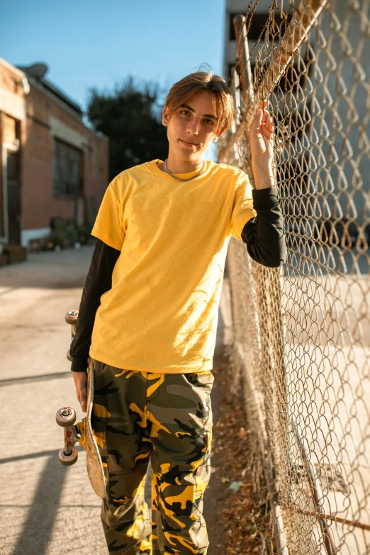 a boy standing next to the fence holding his skateboard