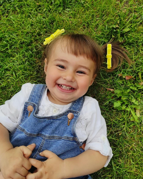 the little girl is smiling and laying in the grass