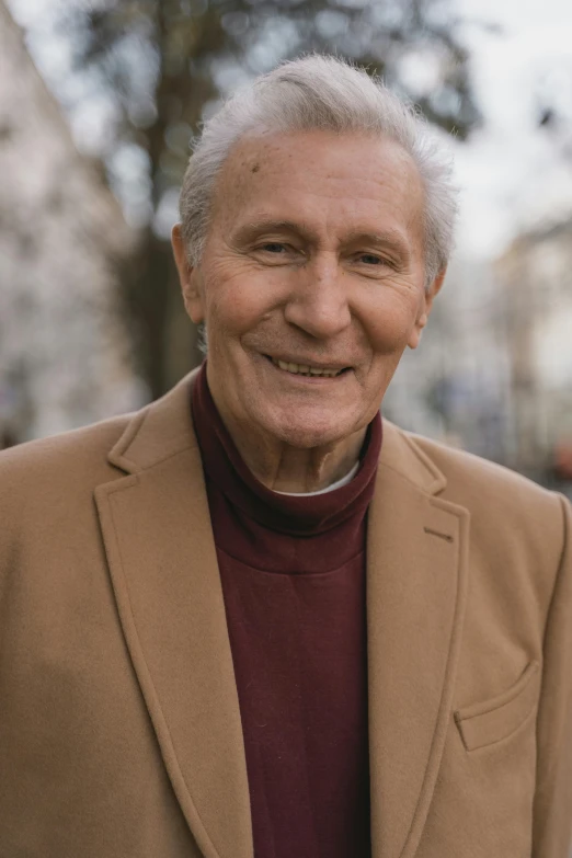 an older man in a brown jacket smiles for the camera