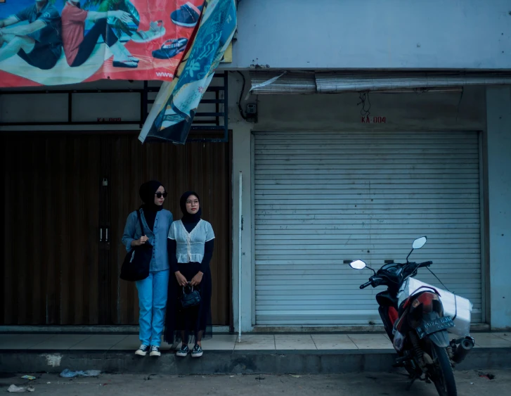 two girls stand next to a parked motor cycle