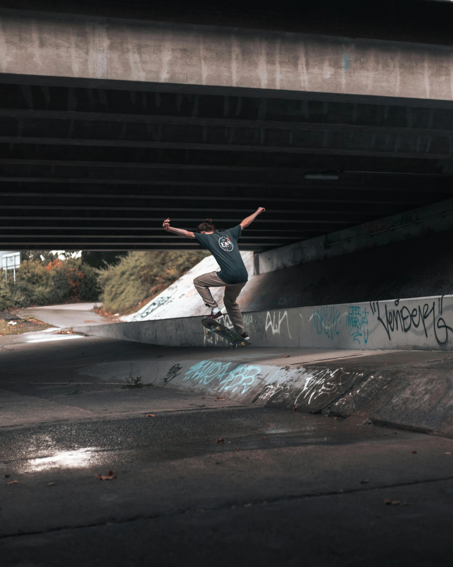 a skateboarder jumps underneath an overpass to do a trick