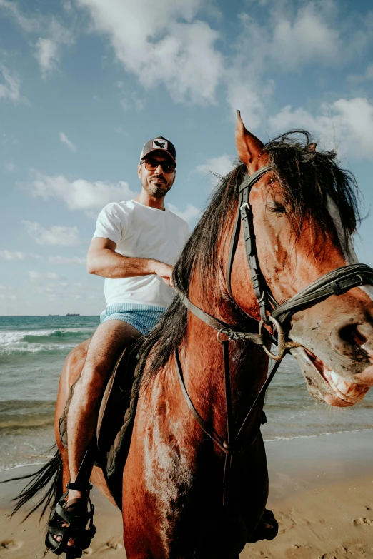 a man riding on the back of a brown horse on a beach