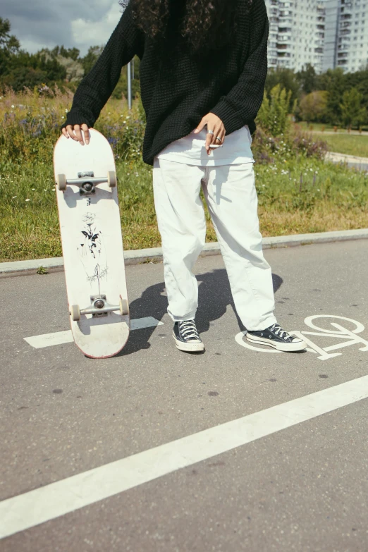 the person with white pants stands beside a skateboard