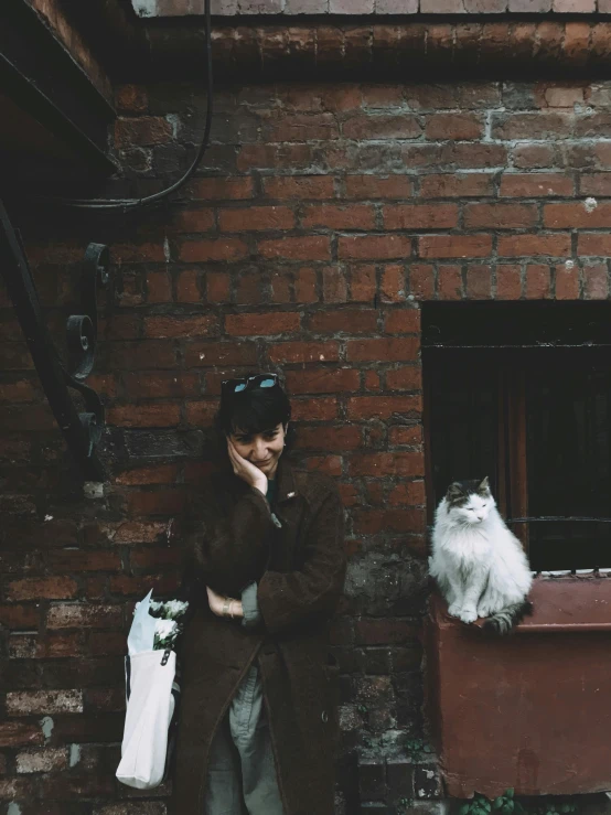 a girl with a hand on her head is standing near a wall and a cat